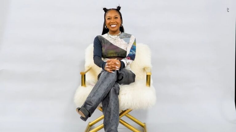 Brooklyn Frost sits smiling on a white fur chair with her legs crossed against a simple studio backdrop