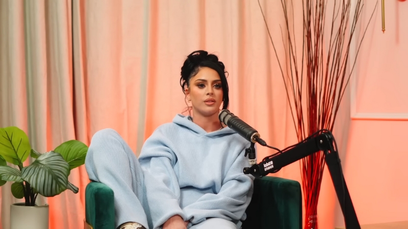 Camilla Araujo speaks into a podcast microphone while wearing a light blue outfit