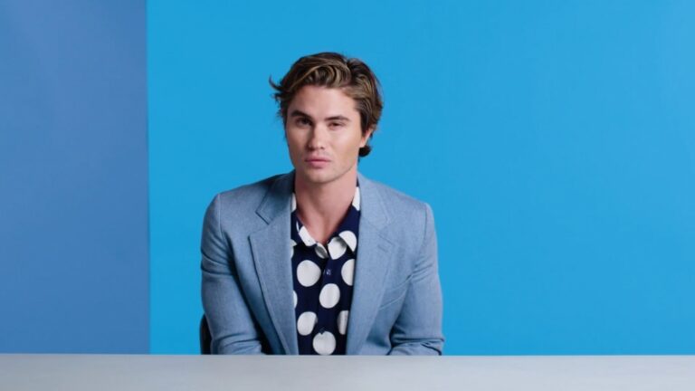 Chase Stokes sits at a table in a light blue blazer and polka dot shirt during an interview