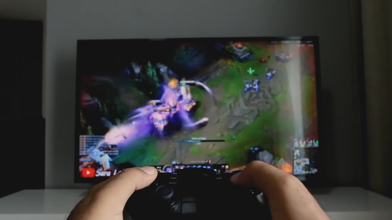 Hands hold a controller while a fast-paced online game plays on a TV screen