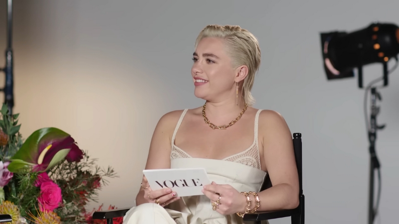 Florence Pugh smiles during a Vogue interview, holding cue cards in a studio setting