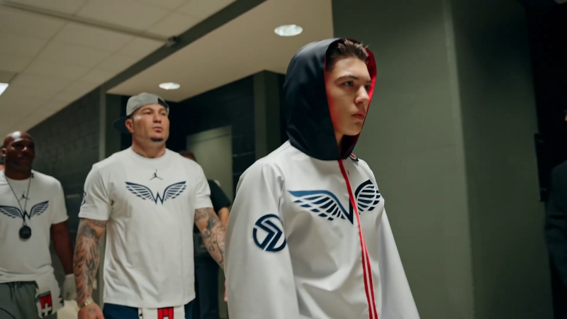 Javon Walton walks toward the boxing ring in his hooded gear with his coaching team following behind