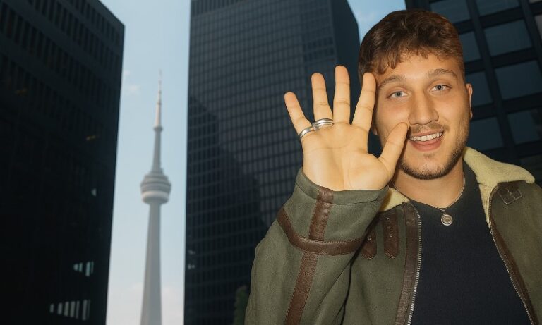 John Abraham Hewson waving at camera, with tall buildings behind him