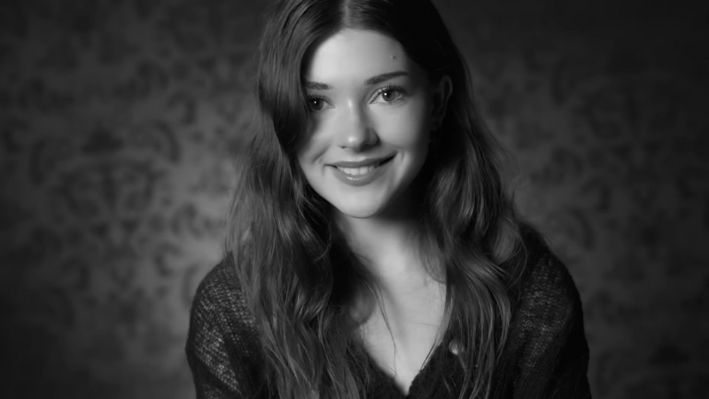 Katie Douglas smiles softly in a black-and-white portrait with long wavy hair against a patterned background