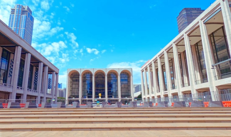 Imposing travertine architecture of Lincoln Center framed by a vibrant, cloud-dappled blue sky in New York City