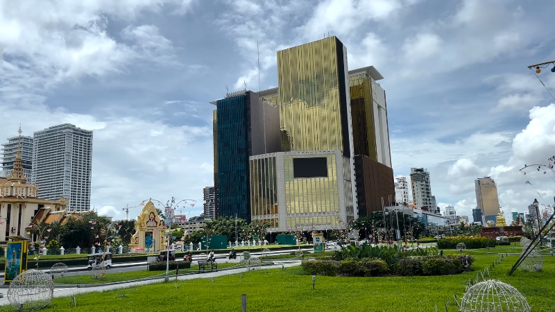 A daytime view of NagaWorld in Phnom Penh with its gold glass towers and surrounding city buildings seen across a public park