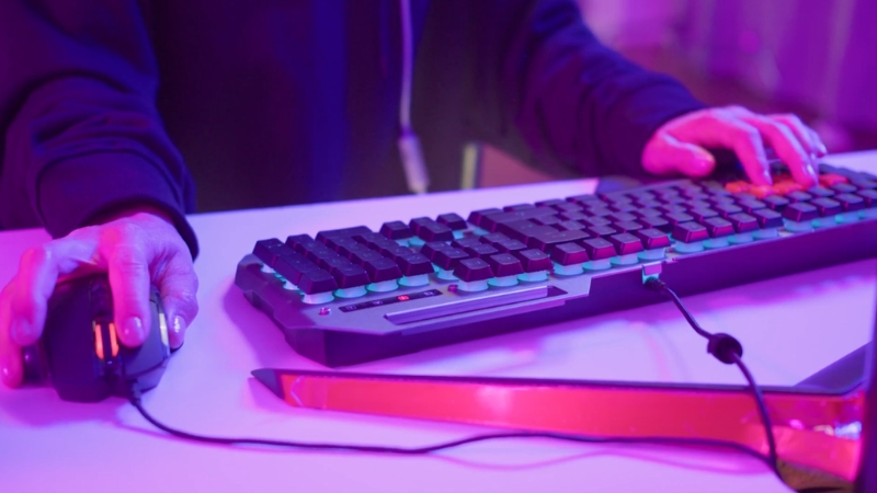 Hands on a gaming keyboard and mouse under purple lighting during online play