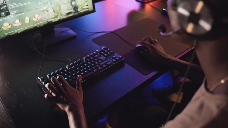 A person uses a keyboard and mouse at a gaming setup with a headset on