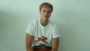 Rudy Pankow sits against a plain light background wearing a white T-shirt