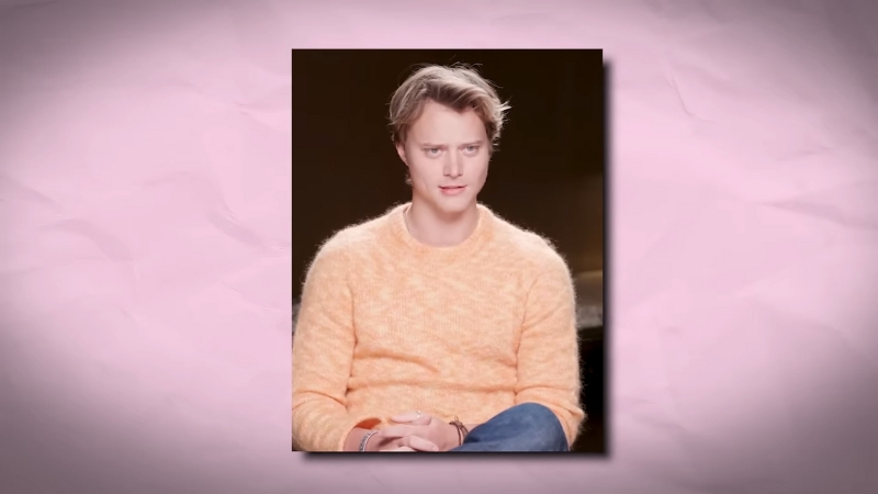 Rudy Pankow sits calmly in a light setting wearing a soft orange sweater
