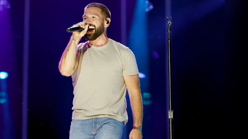 Shay Mooney performs on stage in a casual outfit, holding a microphone and singing to the crowd