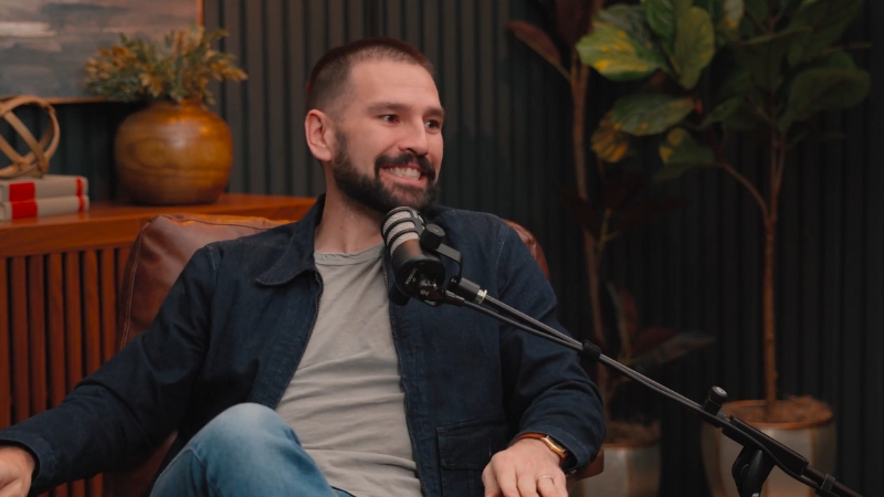 Shay Mooney sits in a studio chair, smiling and speaking into a podcast microphone