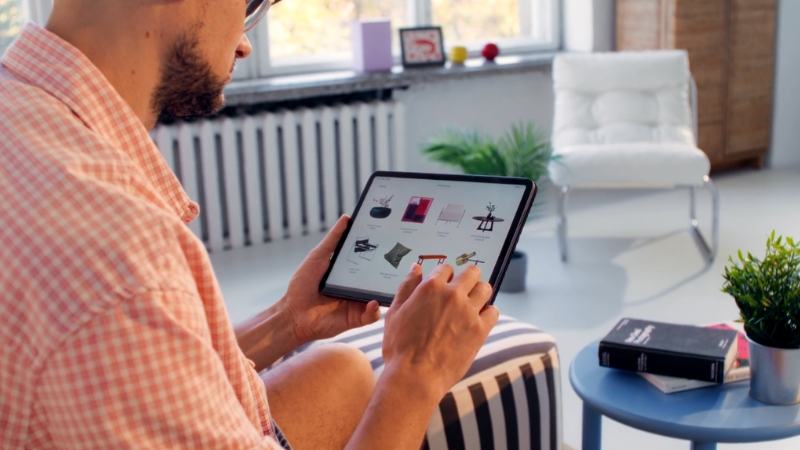 A man browses products on a tablet while sitting in a bright modern room