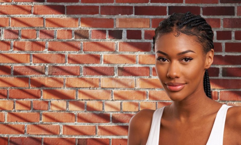 A beautiful Sydney Winbush with braids stands in front of a textured brick wall