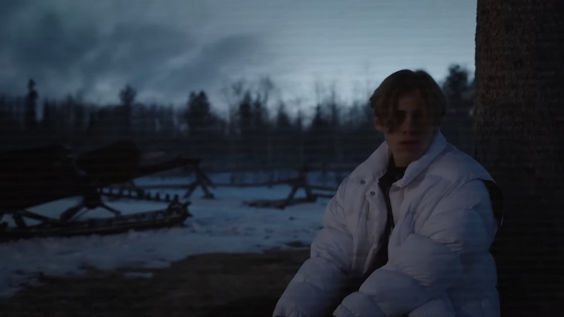 Kid Laroi sits outdoors in a white puffer jacket during twilight
