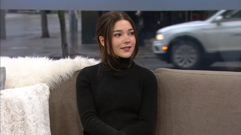 Katie Douglas sits on a studio couch in a black turtleneck, looking to the side during an interview