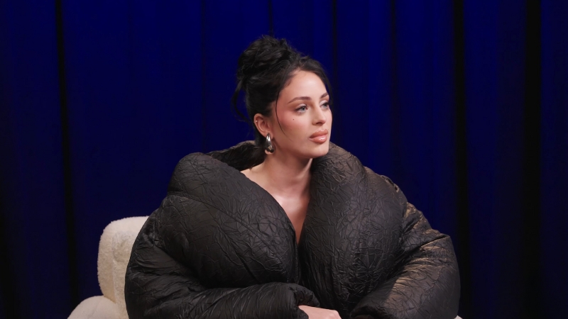 Camilla Araujo sits calmly in a black textured jacket during an interview
