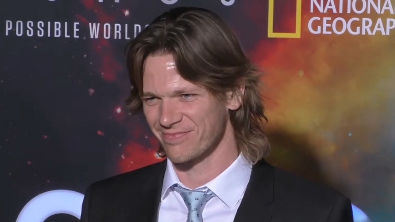 Jon Beavers stands on a red carpet in a suit and tie