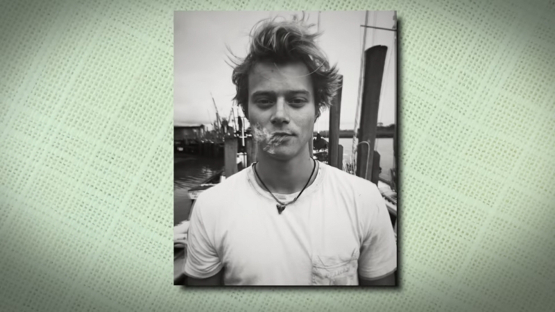 Rudy Pankow stands outdoors near boats in a black-and-white photo