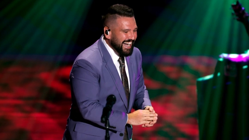 Shay Mooney smiles on stage in a purple suit during a live performance