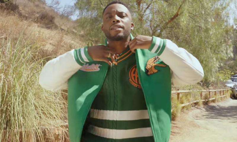Woody McClain wearing a green jacket over a white shirt, smiling at the camera