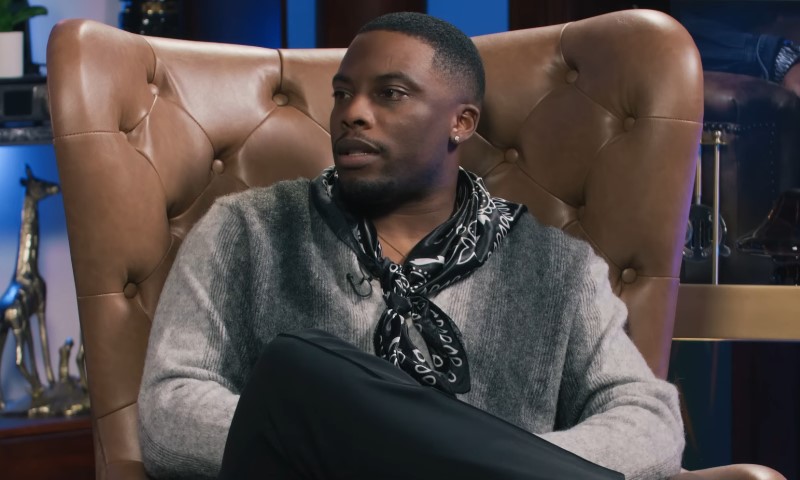 A man named Woody McClain sitting in a chair, wearing a stylish scarf