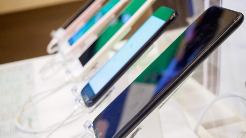 Smartphones are displayed on security stands inside a small mobile shop
