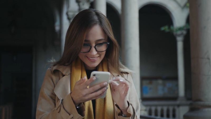 A woman smiles at her phone outside a building