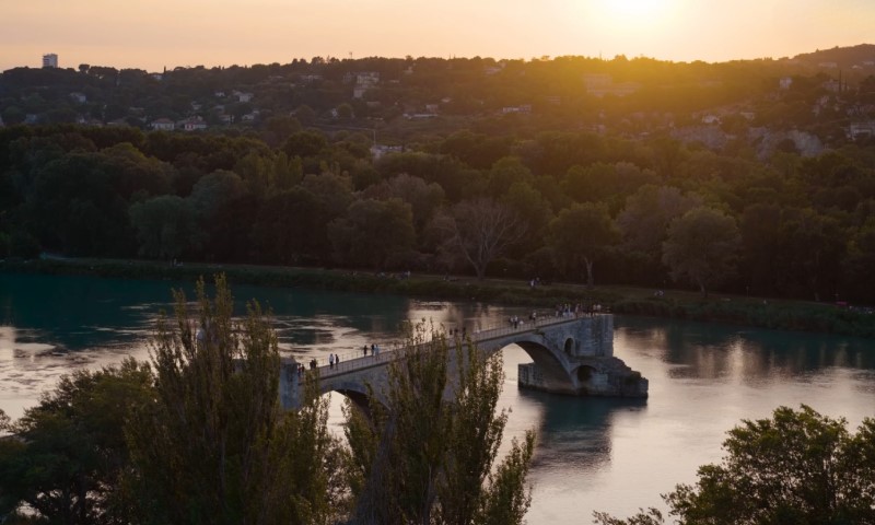 The sun sets over the bridge spanning the river in Avignon