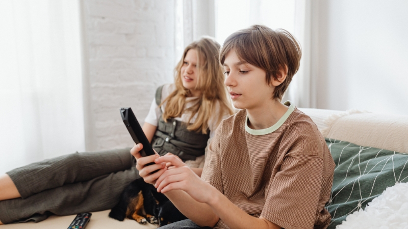 Two kids sit on a couch using a TV remote in a living room
