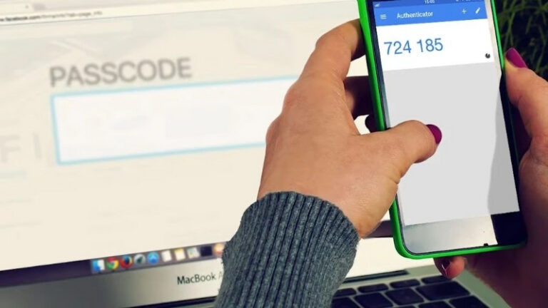 Person enters a login code on a phone authenticator app next to a laptop screen, showin a common 2FA method in use