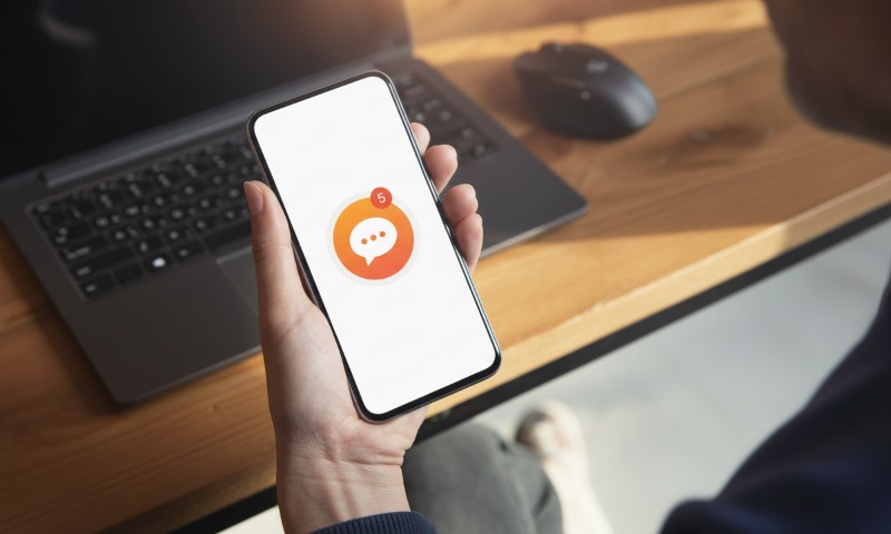 A person holds a smartphone showing an app with a chat bubble icon and a red notification badge displaying