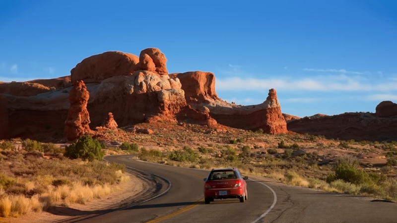 Car driving along a desert road with red rock formations inside Arches National Park