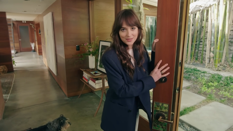 Dakota Johnson opens the wooden front door of her midcentury Hollywood home, with bamboo visible outside