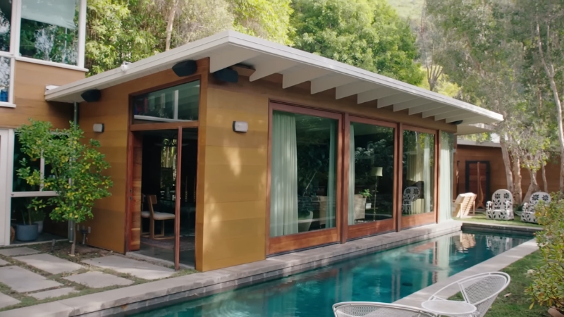 Exterior view of Dakota Johnsonโs midcentury Hollywood home with large glass doors opening to a narrow pool and surrounding greenery