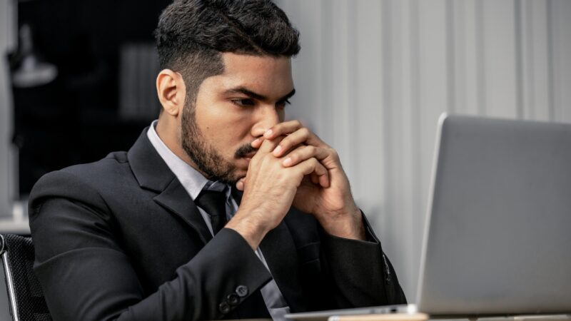 A concerned leader sits at a laptop with hands near his face, showing early leadership symptoms that signal burnout