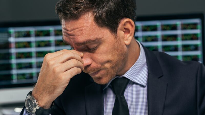A stressed business leader holds his forehead in front of screens, showing signs of founder burnout