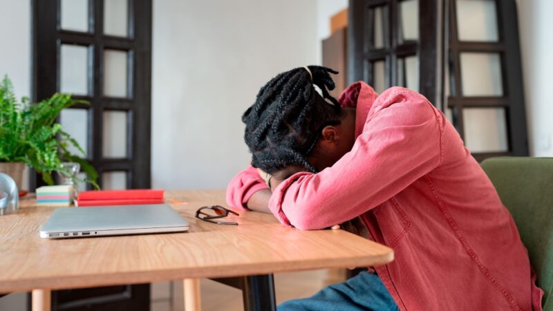 A founder rests his head on a desk beside a laptop, showing operational inefficiencies linked to founder burnout