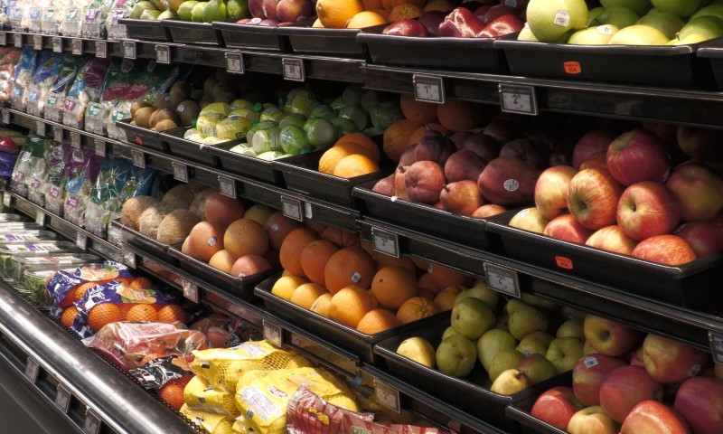 Grocery store produce section with neatly arranged fruits like apples, oranges, and pears in black trays