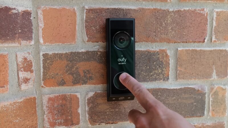 Eufy video doorbell mounted on a brick wall as a person presses the button