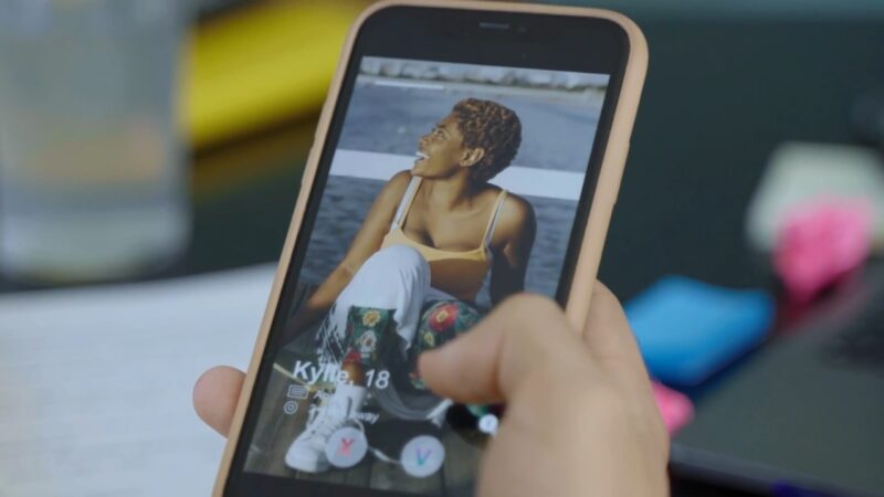 Hand swiping on a Bumble dating profile showing a young woman on a phone screen