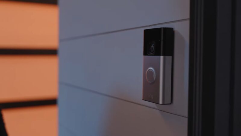 Modern video doorbell mounted next to a front door with camera and button visible