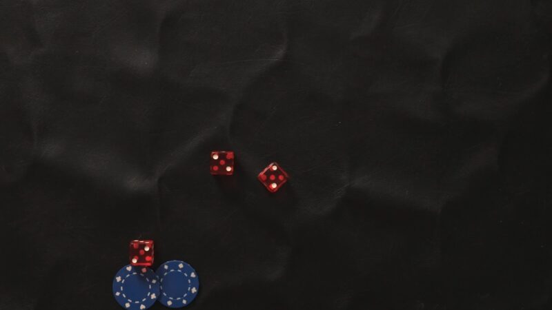Red dice and blue chips sit on a dark table during a Cee-Lo game