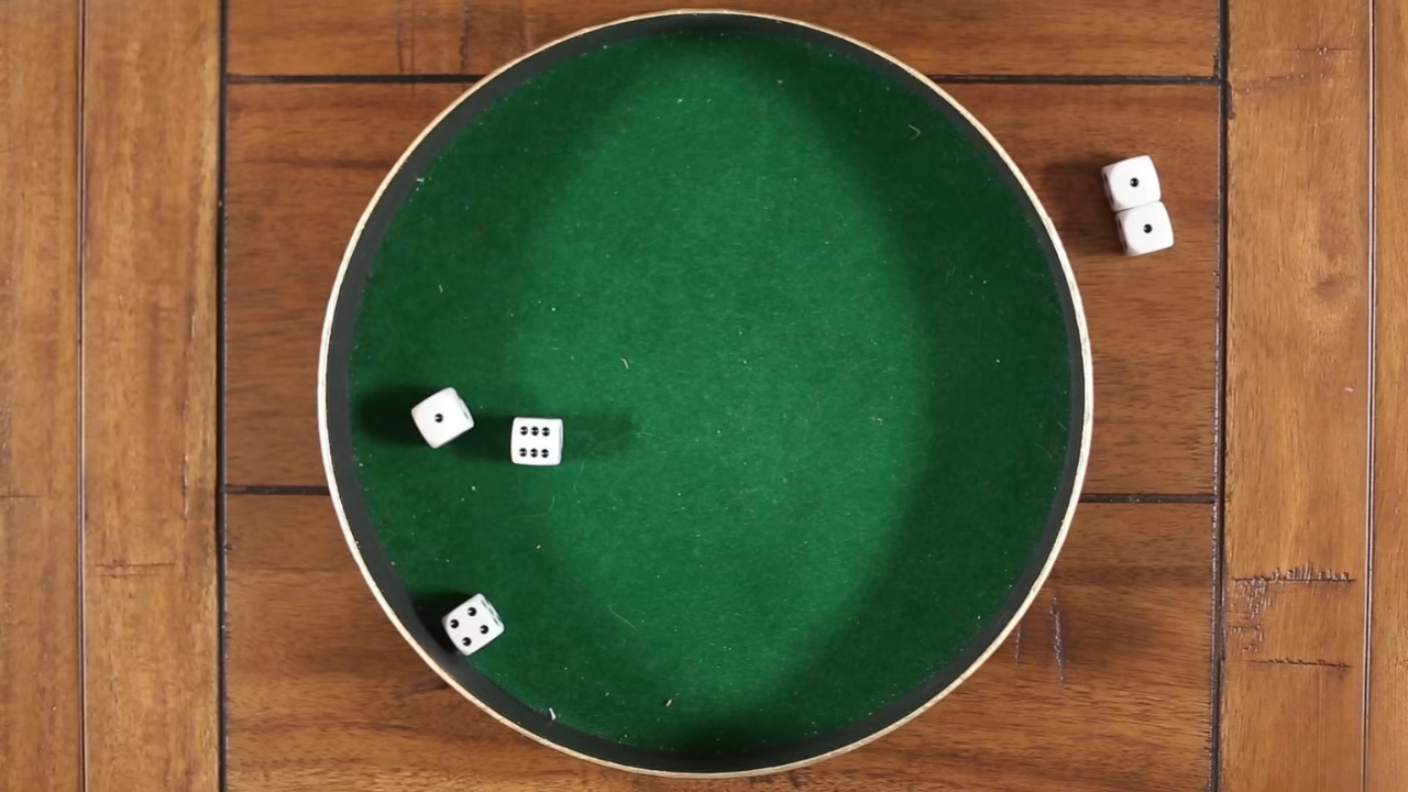 Dice games are set up with white dice on a green felt tray and wooden table