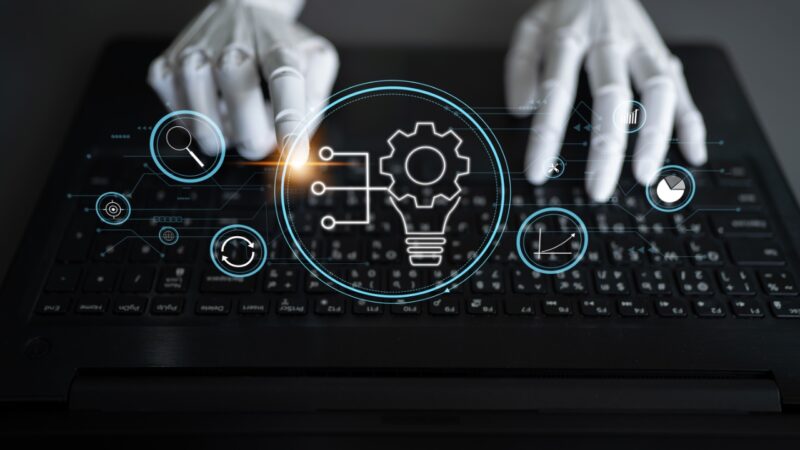 Hands use a laptop with digital icons for AI product improvement and performance tracking