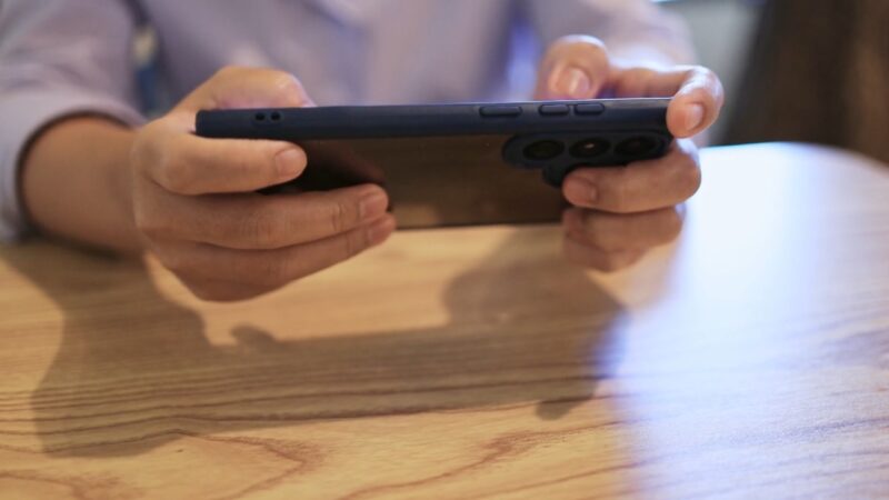 A person uses a smartphone held sideways at a wooden table