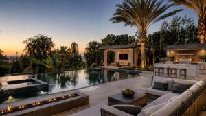 Luxury celebrity-style backyard with infinity pool, cabana, outdoor kitchen, palm trees, fire feature and modern lounge area.