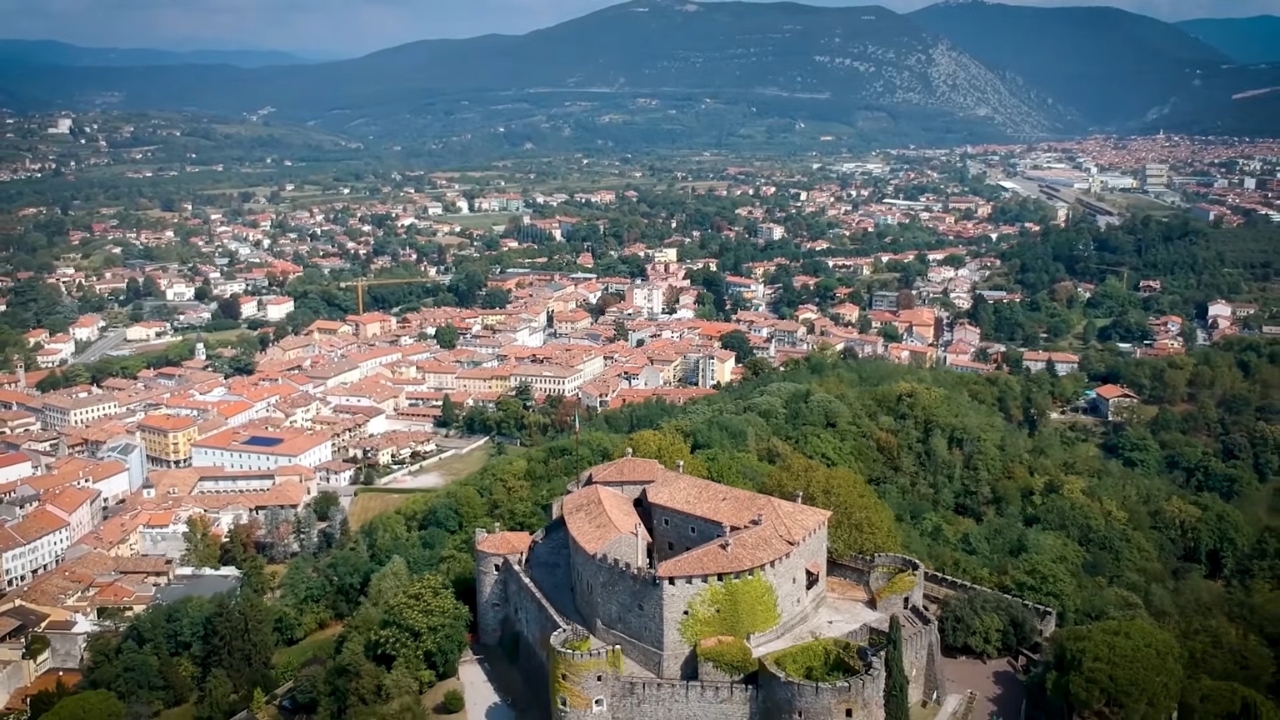 Historic Italian town with a stone fortress and mountains in the background.