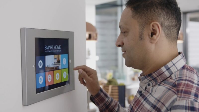 Man uses a wall-mounted smart home control panel.