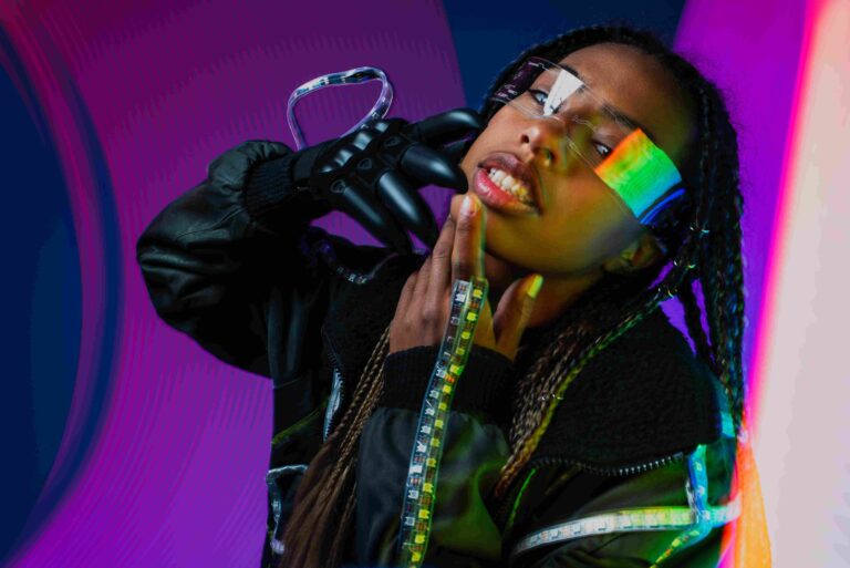 DTF Technology - Fashion model wearing futuristic black clothing, transparent accessories, and reflective eyewear against a colorful background.